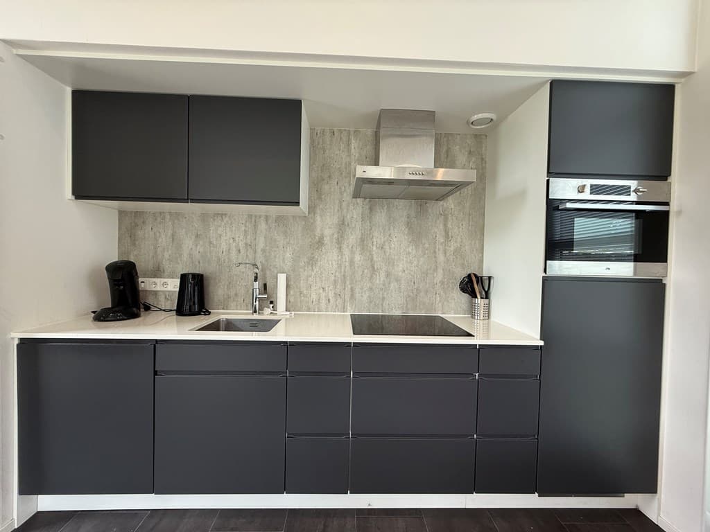 Moderne keuken met donkergrijze kasten, een inductiekookplaat, afzuigkap en inbouwapparatuur in een lichte ambiance