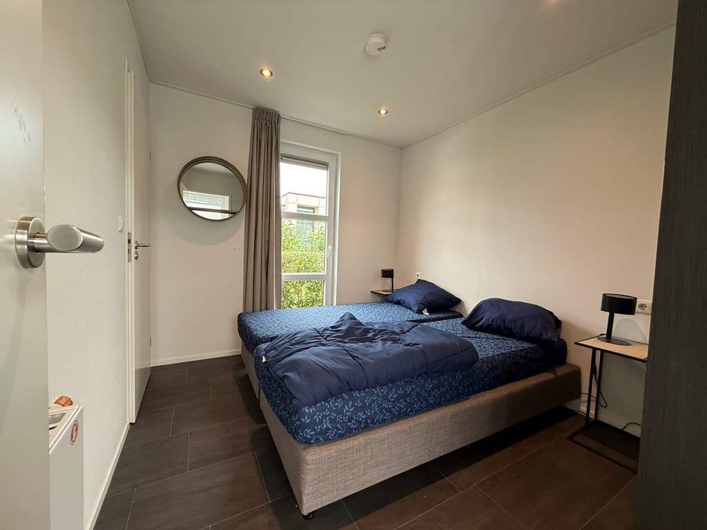 Slaapkamer met tweepersoonsbed, nachtkastjes en raam met uitzicht op groen.