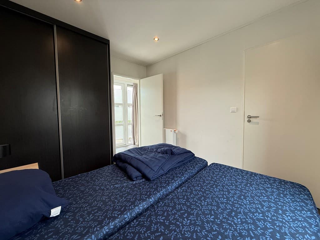 Slaapkamer met een tweepersoonsbed, grote kast en toegang tot een balkon via een deur.