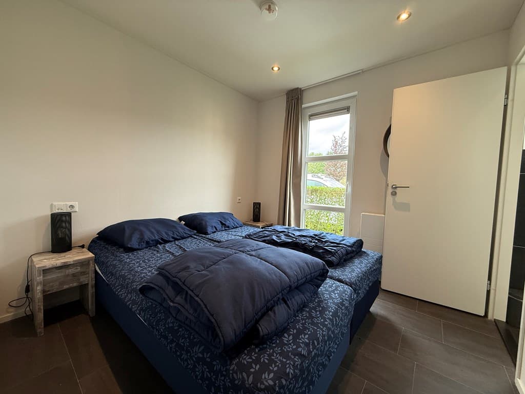 Slaapkamer met een tweepersoonsbed, nachtkastje en een raam met uitzicht op de tuin.