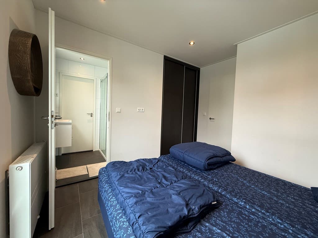 Slaapkamer met een tweepersoonsbed, toegang tot een badkamer en een kastwand zichtbaar aan de achterzijde.