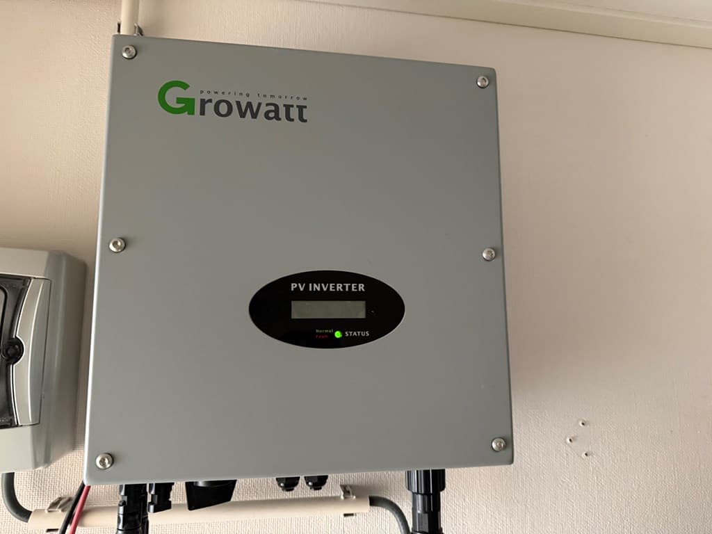 Zicht op een grijze PV omvormer aan de wand met een statusindicatie en aansluitingen onderin.