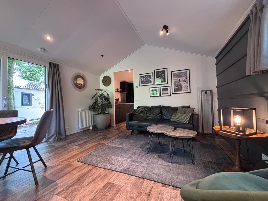 Modern interieur met een zithoek, houten vloeren en een eettafel, lichtinval van ramen en schilderijen aan de muur