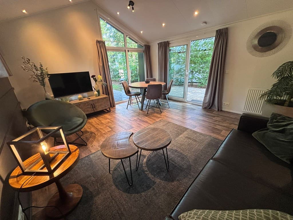 Moderne woonkamer met zithoek, eettafel en grote ramen met uitzicht op de groene omgeving
