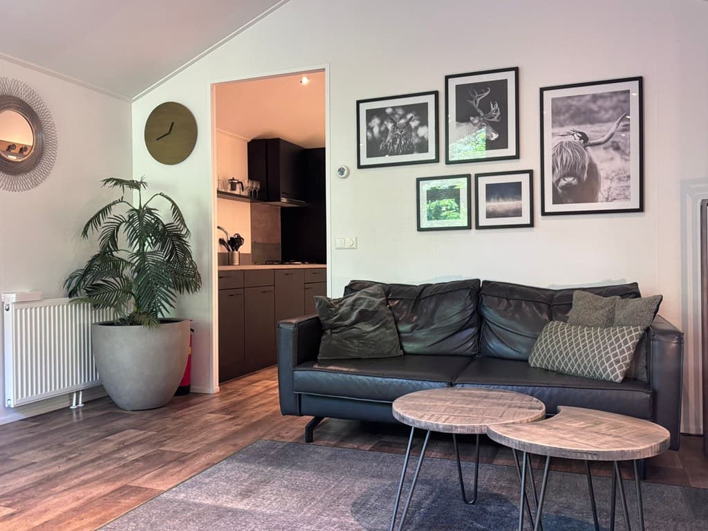 Zithoek met een donker leren bank, twee ronde tafels en een wand met ingelijste afbeeldingen en een klok