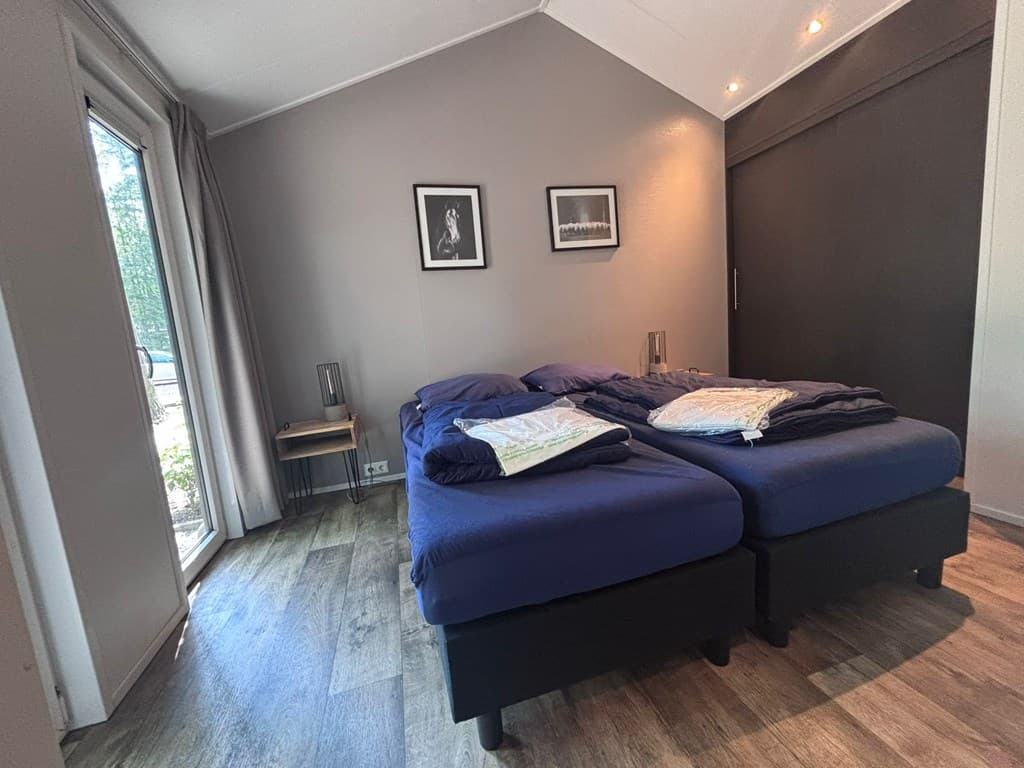 Slaapkamer met twee aparte bedden, een glazen deur naar buiten en kunst aan de muur.