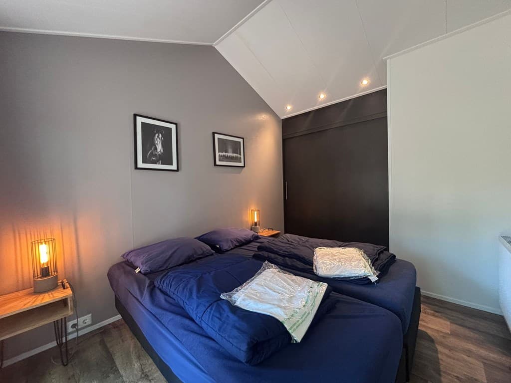 Slaapkamer met twee eenpersoonsbedden, schilderijen aan de muur en sfeerverlichting naast de bedden.