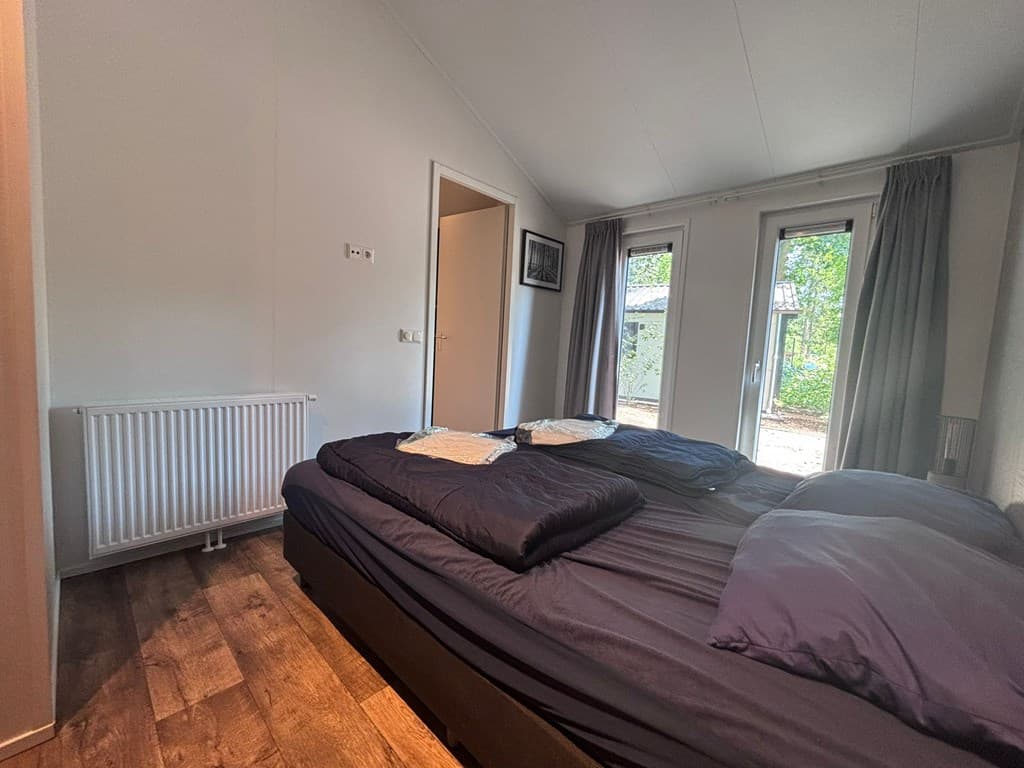 Slaapkamer met tweepersoonsbed, ramen naar buiten en houten vloer in EuroParcs Resort De Utrechtse Heuvelrug.