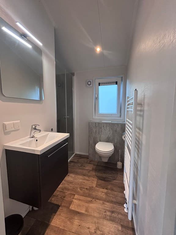 Moderne badkamer met douche, wastafel, toilet en handdoekenradiator in lichte kleuren en houten vloer