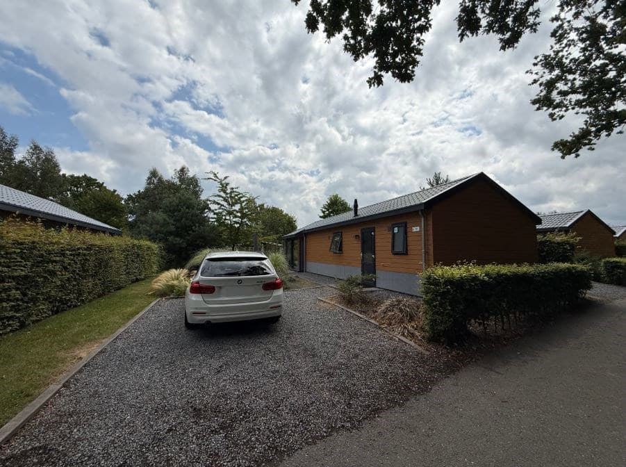 Buitenaanzicht van een woning met een wit voertuig op een grindpad, omgeven door groen en een goed onderhouden tuin