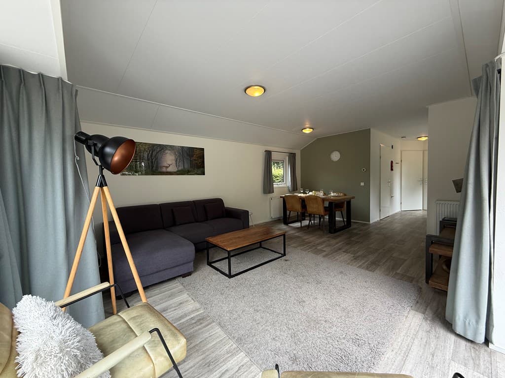 Moderne woonkamer met zithoek, eettafel en veel natuurlijk licht door ramen en deuren.