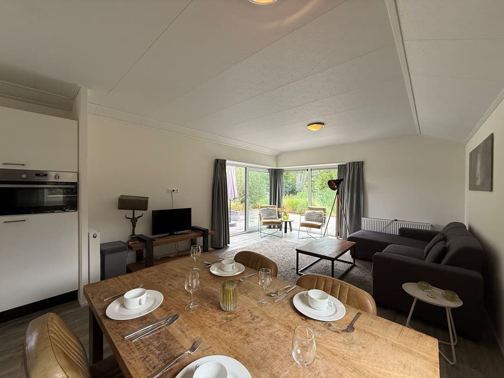 Ruime woonkamer met eetruimte, moderne bank en grote ramen met uitzicht op de tuin.