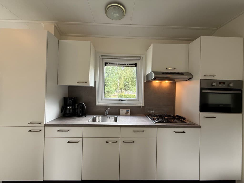 Moderne keuken met inbouwapparatuur, spoelbak en raam met uitzicht op de aangrenzende natuur.