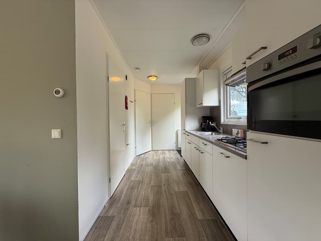 Moderne keuken met rechte opstelling en witgekleurde kasten, lichte vloer en deur naar een andere ruimte.