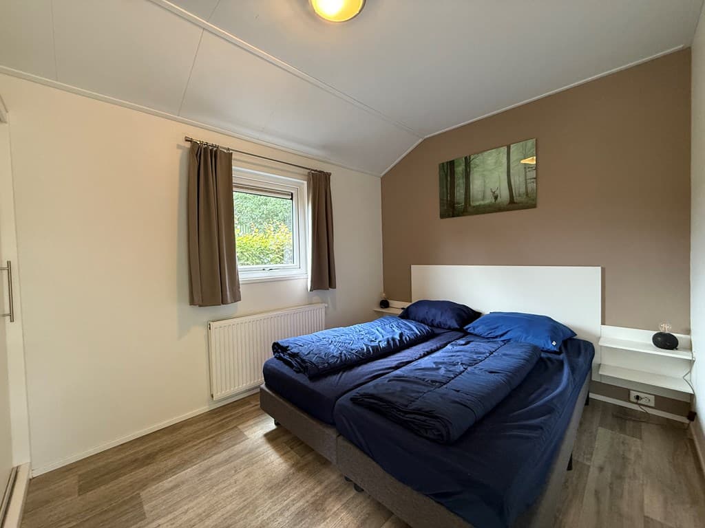 Slaapkamer met twee eenpersoonsbedden, een raam met gordijnen en een schilderij aan de muur.