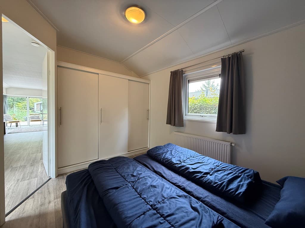 Slaapkamer met twee éénpersoonsbedden, een grote kast en een raam met uitzicht op de buitenruimte.
