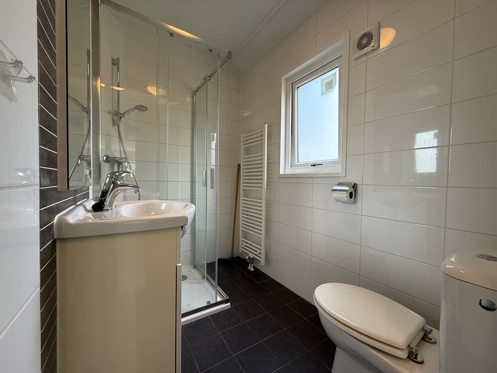 Moderne badkamer met douche, wastafel, toilet en handdoekenradiator in lichte tegels en donkere vloertegels