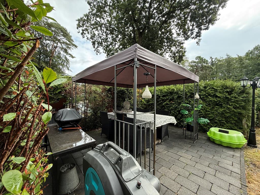 Overdekte buitenruimte met een tafel, stoelen en groene omheining op Camping De Konijnenberg in Harderwijk.