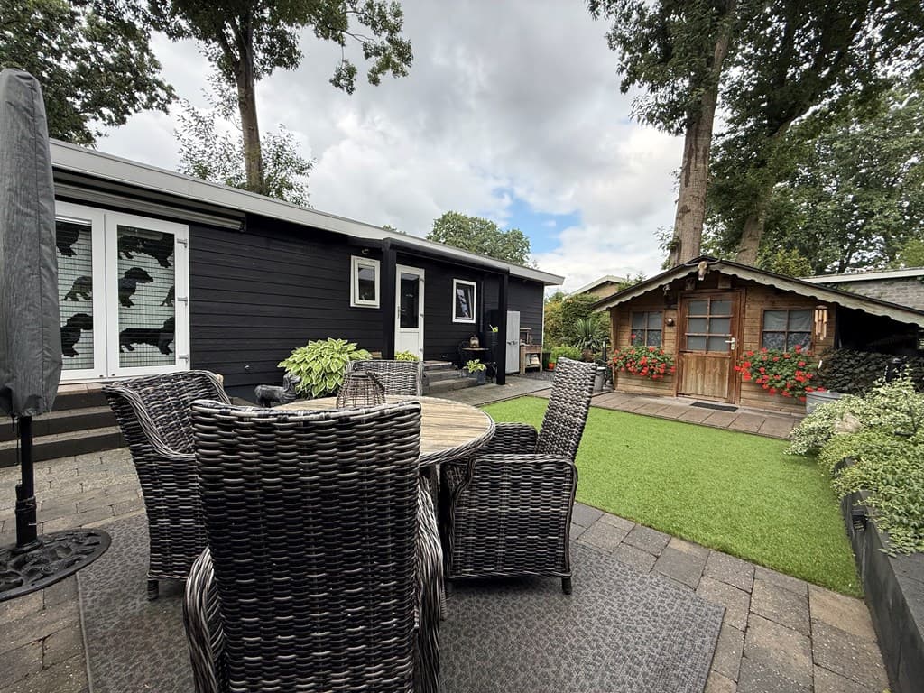 Een recreatiewoning met een terras en tuinmeubilair, een houten chalet met bloembakken en groene graszones.