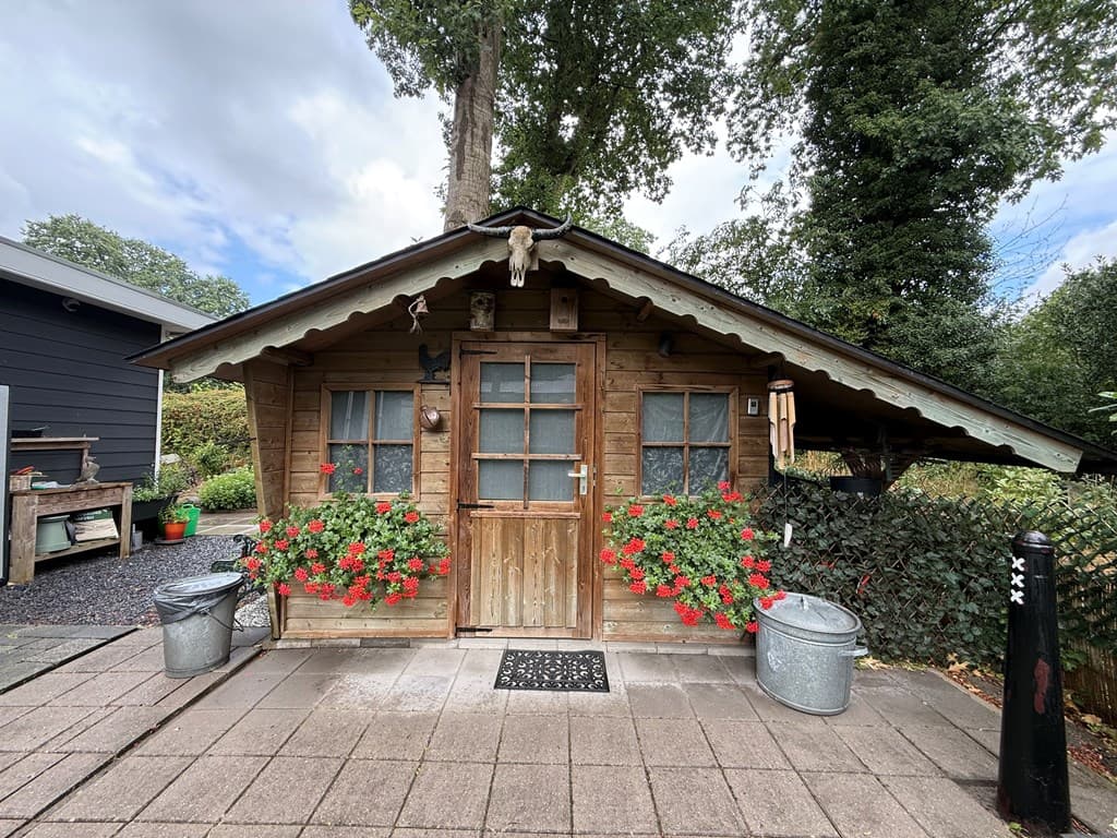 Houten recreatiewoning met bloemen en decoratieve elementen aan de voorzijde, omringd door groen en grindpaden
