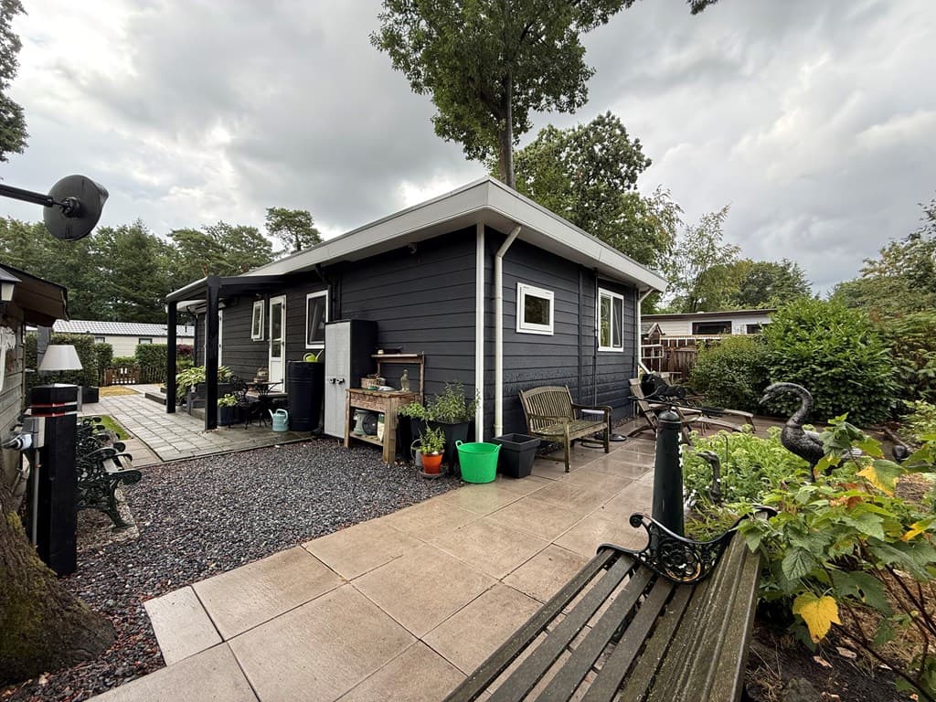 Zijaanzicht van een recreatiewoning met een betegeld terras, plantenbakken en een groene tuin rondom