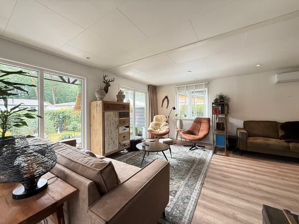 Ruim en licht interieur van een recreatiewoning met moderne meubels, grote ramen en een zithoek met verschillende stoelen