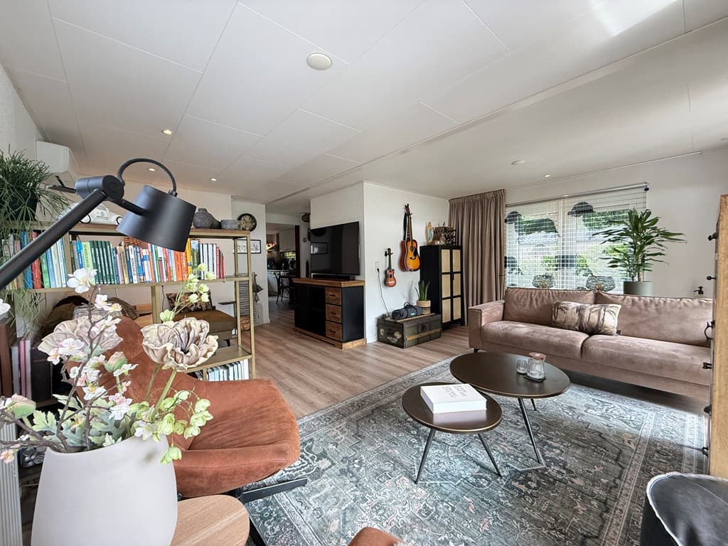 Ruime woonkamer met zithoek, boekenplank, tv-kast en grote ramen met uitzicht op de tuin