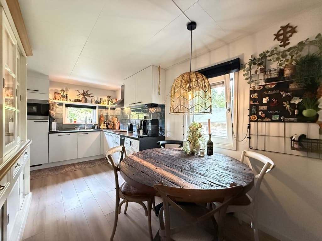 Gezellige keuken met een ronde houten eettafel, moderne apparatuur en wanddecoraties met planten en kruiden.