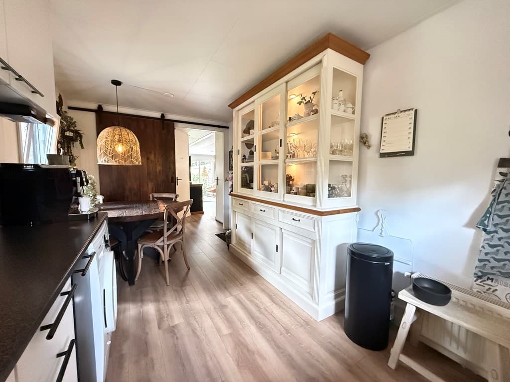 Gezellige inrichting met een eettafel, kast en keuken, lichte kleuren en houten accenten in een recreatiewoning