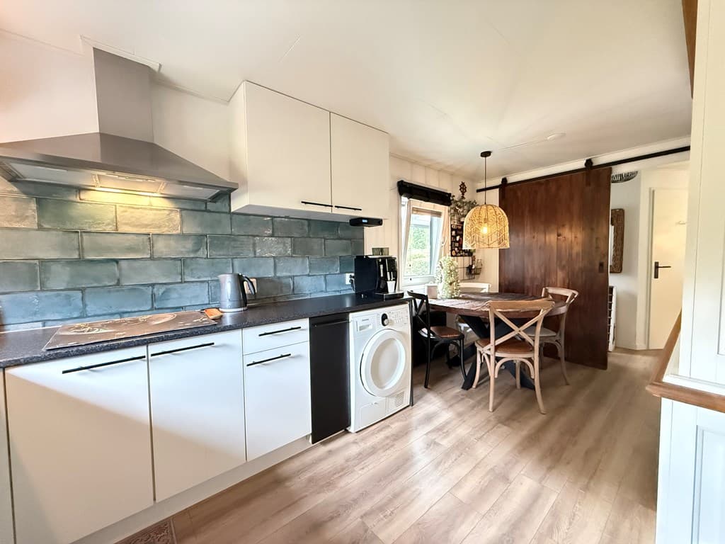 Keuken met witmeubels, een eettafel met stoelen en een houten wandpaneel in een recreatiewoning