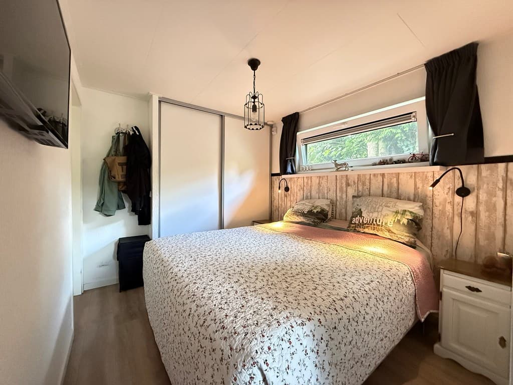 Slaapkamer met groot bed, wanddecoratie en raam met uitzicht naar buiten, kledingrek en televisie aan de muur
