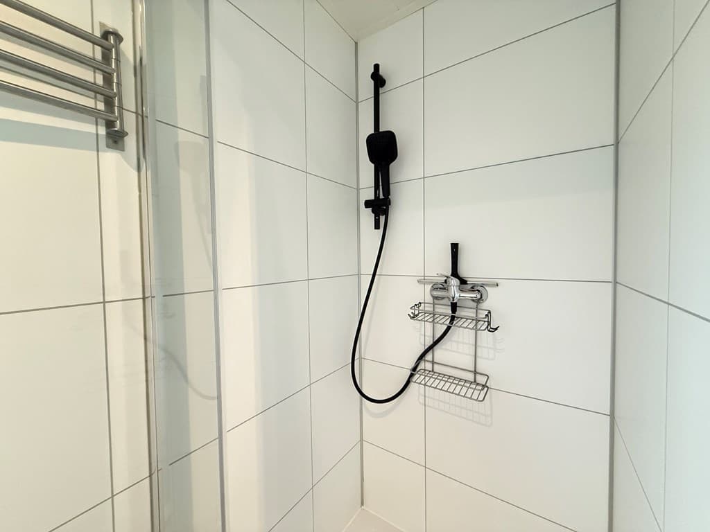 Douchehoek met witte wandtegels, douchekop aan wand en rekje voor toiletartikelen