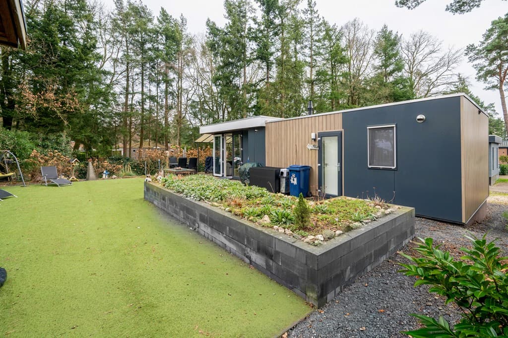 Recreatiewoning met een moderne uitstraling, omgeven door groen en een aangelegde tuin met grind en gras.