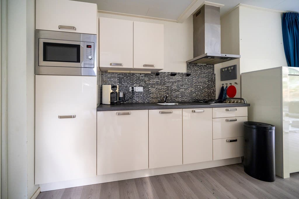 Keuken met moderne kastjes, een oven, kookplaat en een zwarte werkblad met mozaïek achterwand en koelkast