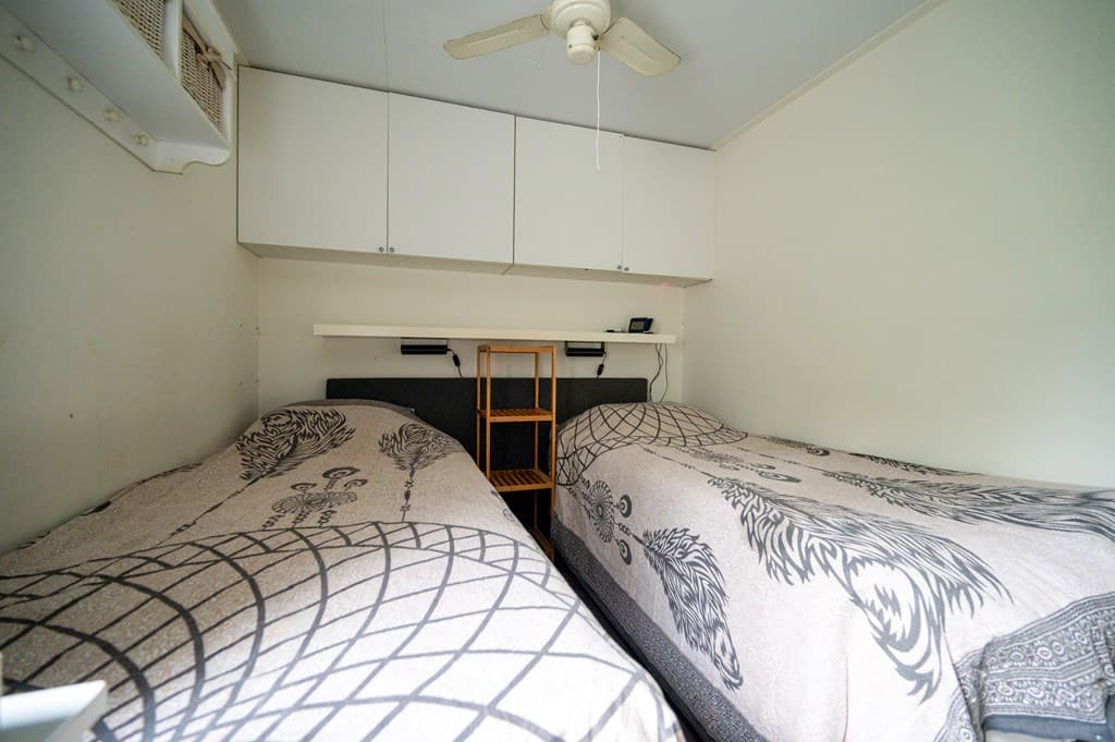 Slaapkamer met twee eenpersoonsbedden, een plafondventilator en bovenkasten tegen de muur