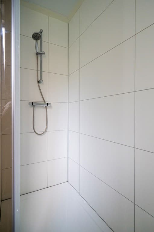 Inloopdouche met lichte wandtegels en een wanddouchekop in een recreatiewoning.
