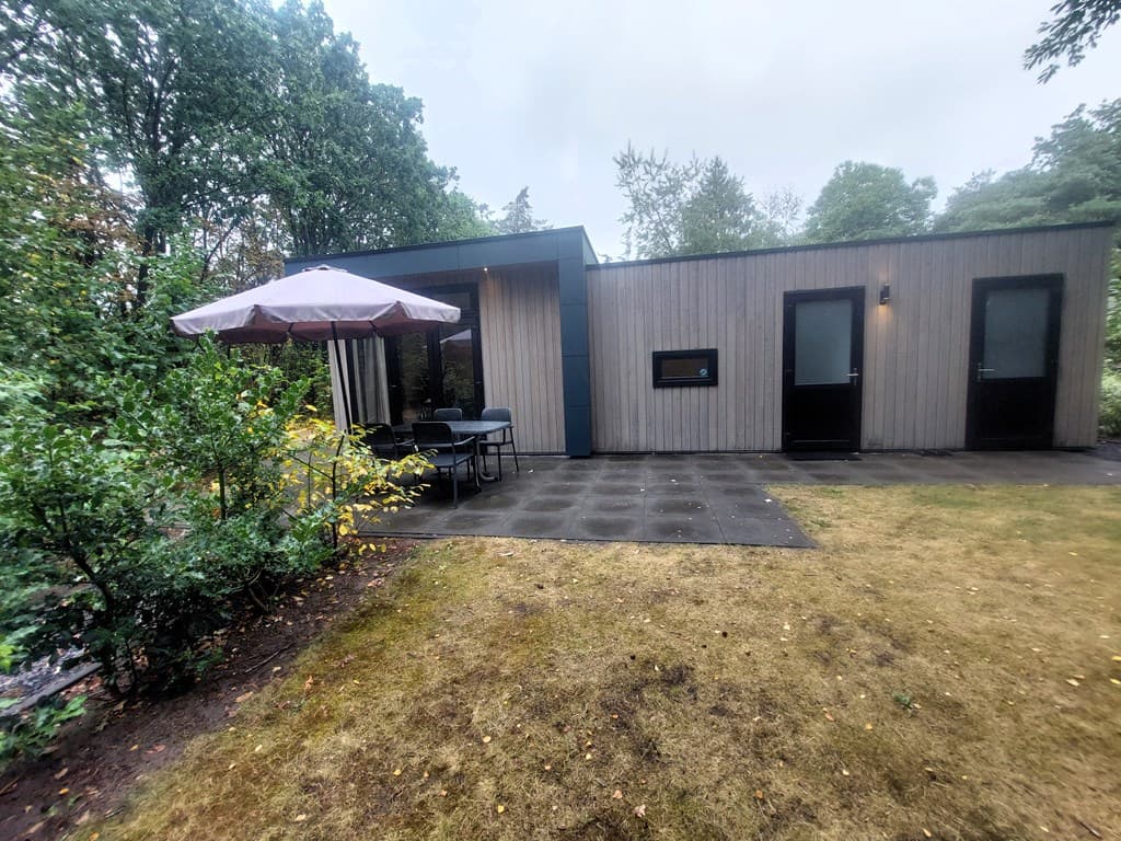 Recreatiewoning met overdekt terras en tuinmeubilair, omgeven door groen en bomen in EuroParcs De Zanding.