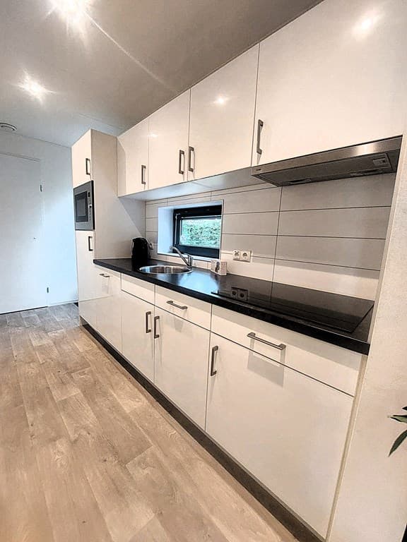 Moderne keuken met witte kasten, zwart aanrecht en raam met uitzicht op buitenruimte.