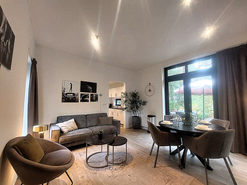 Moderne woonkamer met zithoek, eettafel en grote ramen met uitzicht op het terras en groene omgeving
