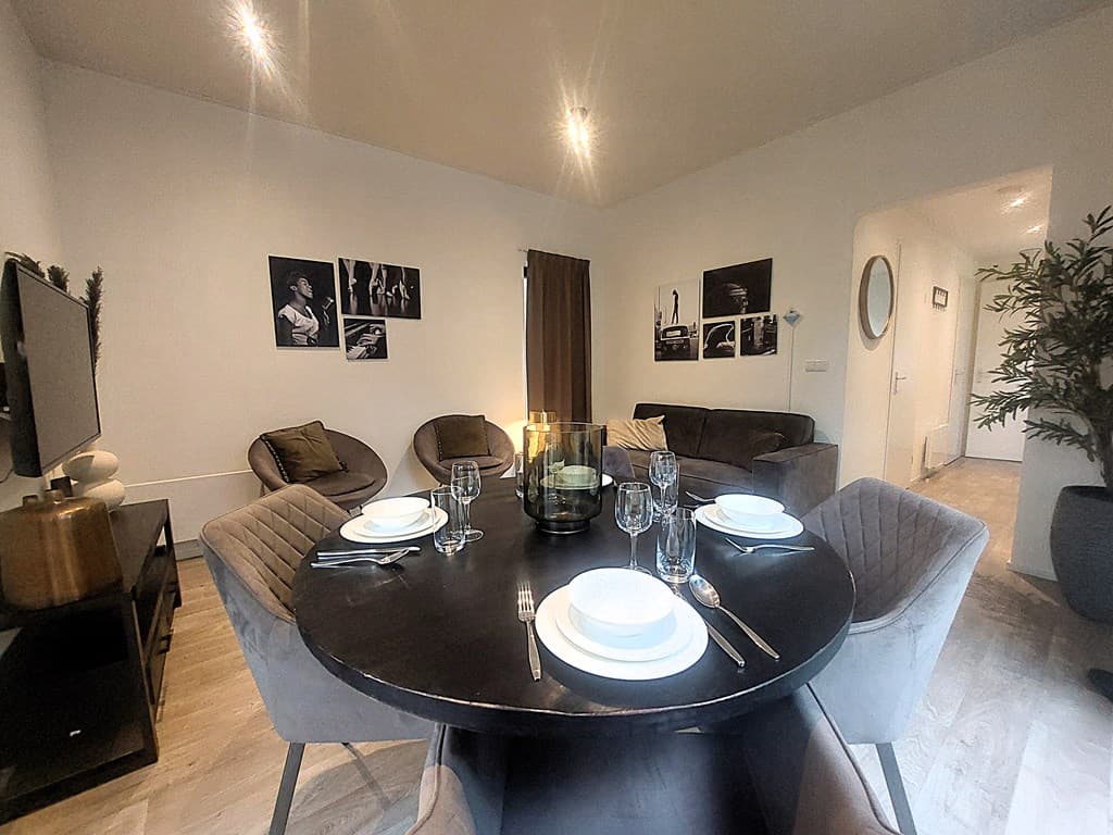 Eetkamer met ronde tafel, vier stoelen, decoratieve kunst aan de muur en een bank in een lichte ruimte