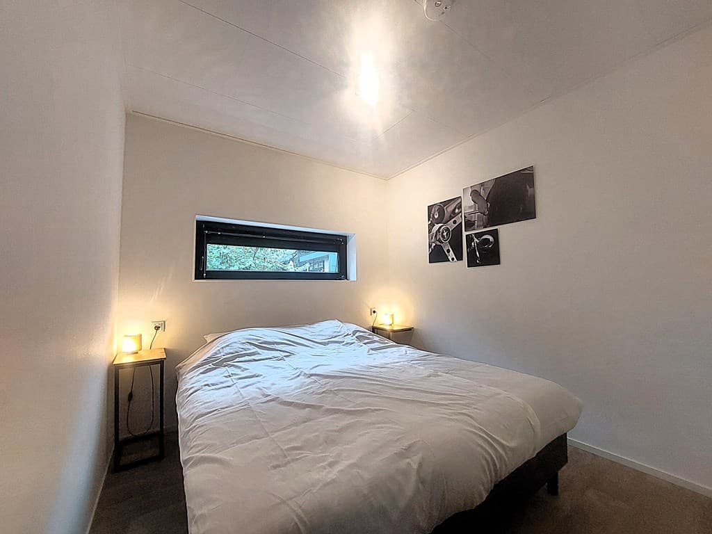 Slaapkamer met een tweepersoonsbed, nachtkastjes met lampen en een klein raam met uitzicht op de natuur