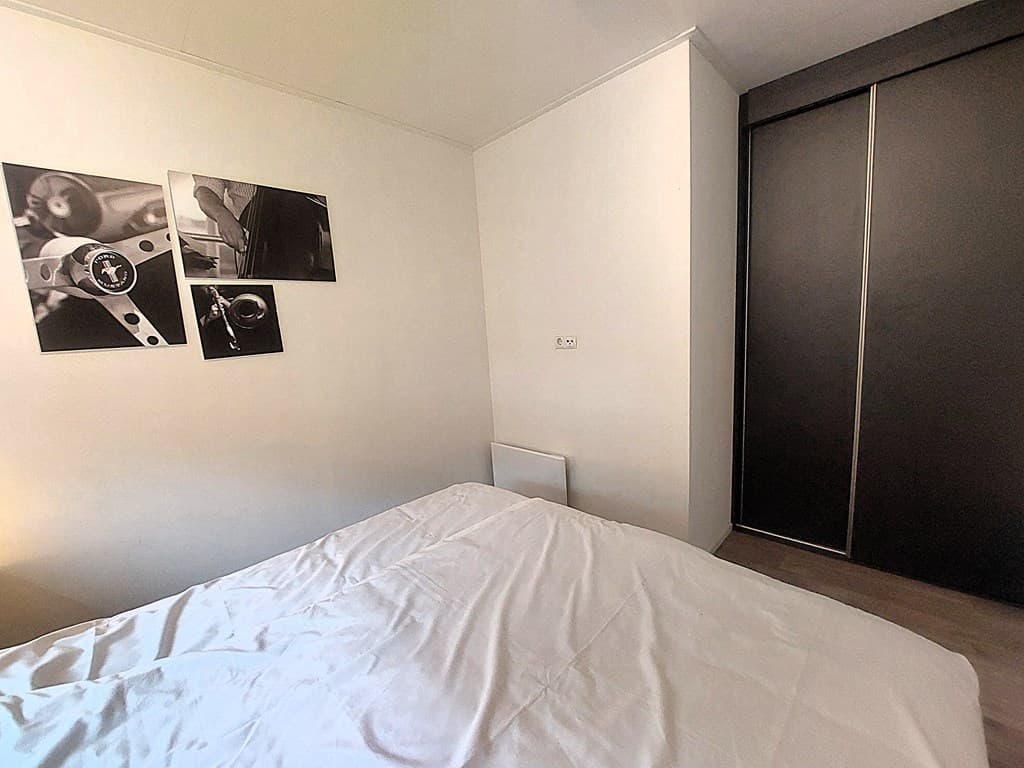 Slaapkamer met een bed en zwart kledingkast, twee zwart-wit foto’s aan de muur zichtbaar