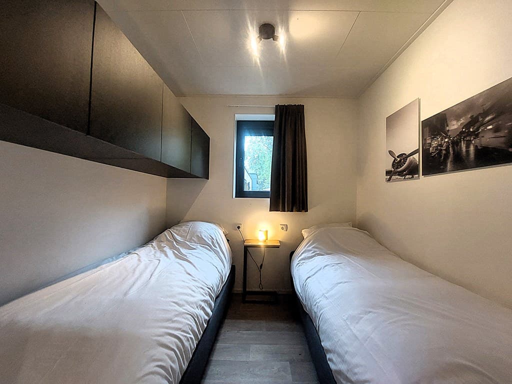 Slaapkamer met twee eenpersoonsbedden, nachtkastje met lamp, wandkasten en een raam met uitzicht naar buiten