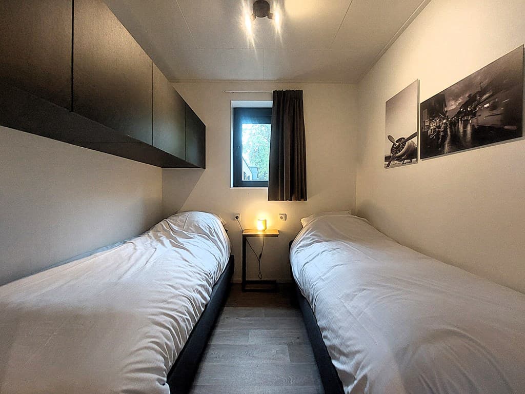 Slaapkamer met twee eenpersoonsbedden, nachtkastje met lamp en een raam met uitzicht naar buiten