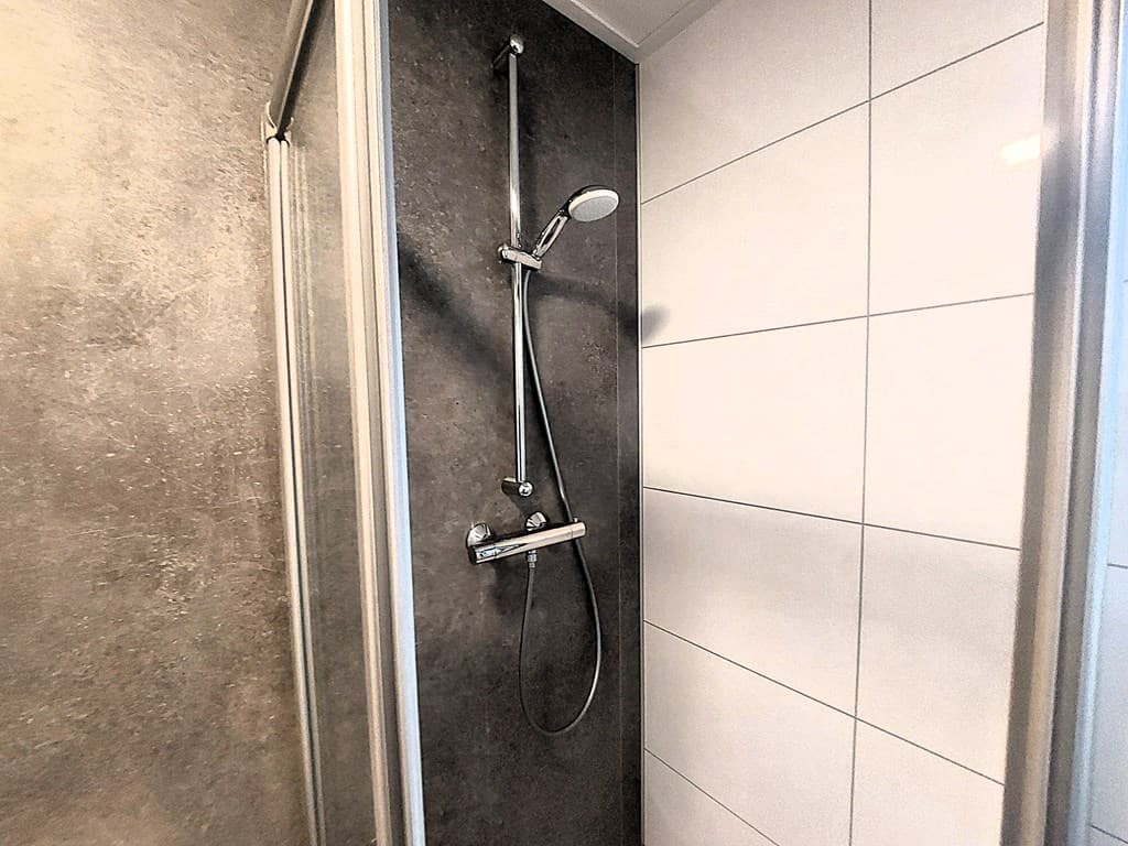Moderne douche met een wand van grijze en witte tegels in een recreatiewoning