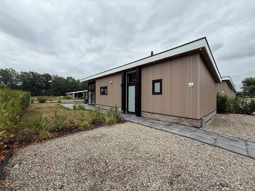 Moderne recreatiewoning met een houten gevel, omgeven door gravel en groen, gelegen in een rustige omgeving