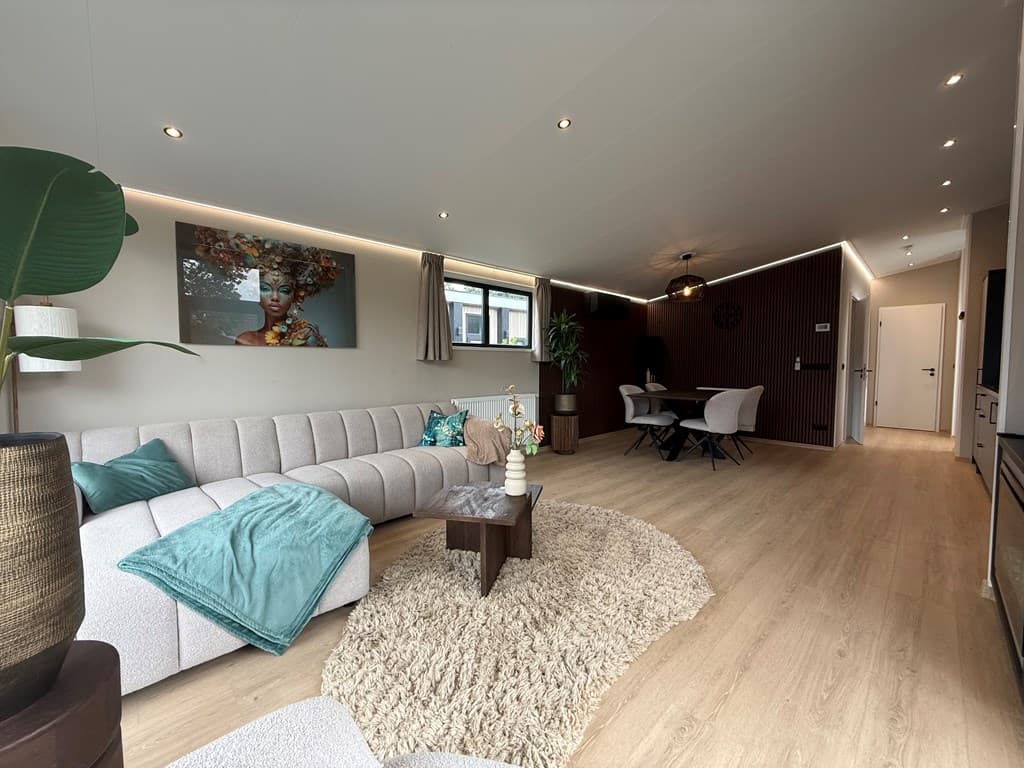 Lichte woonkamer met een hoekbank, eettafel, decoratieve plant en kunst aan de muur.