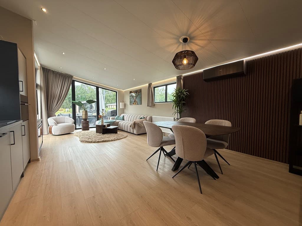 Lichte woonkamer met zithoek, eethoek, grote ramen en moderne inrichting in neutrale kleuren.