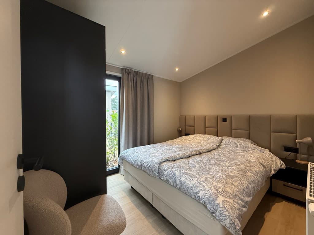 Slaapkamer met tweepersoonsbed, nachtkastjes, stoel en raam met zicht op buiten.
