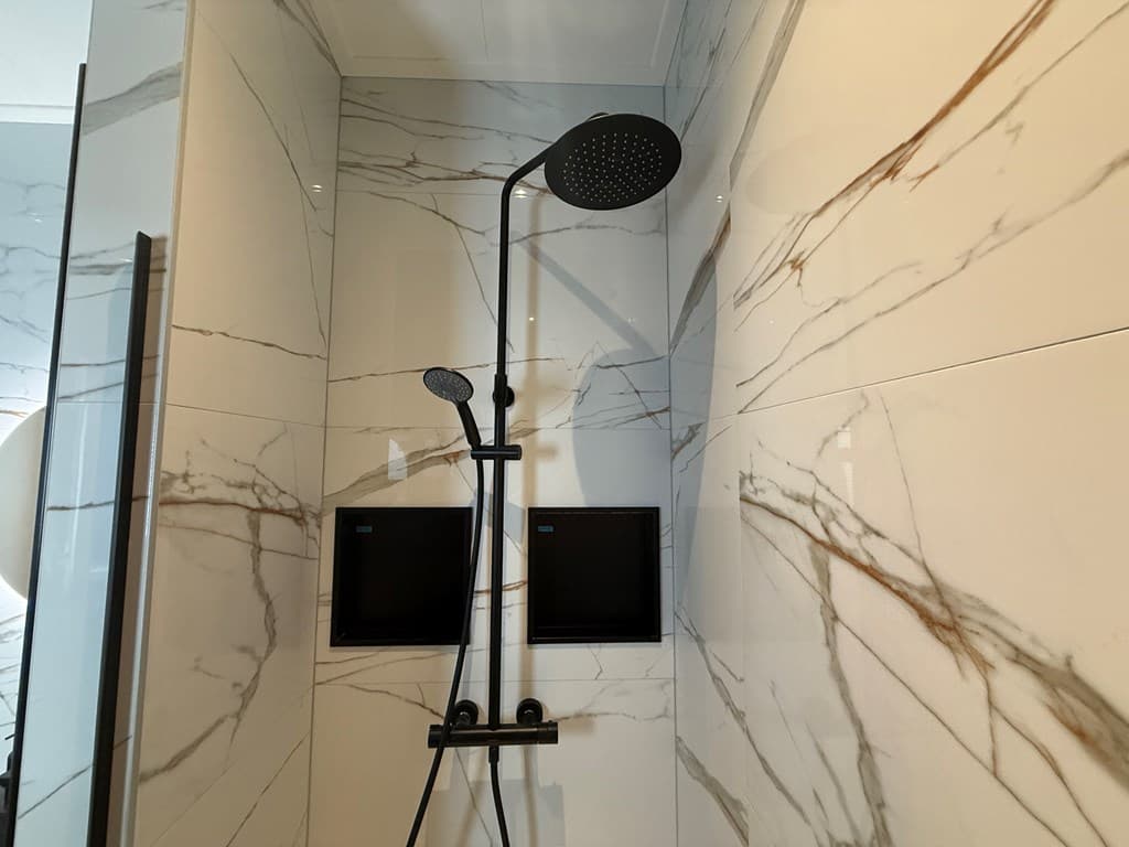 Moderne douche met regendouche en handdouche, afgewerkt met marmeren wandtegels en twee wandkasten.